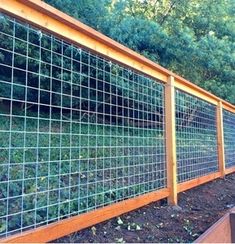 a wooden fence with metal grids on the top and bottom, in front of some trees