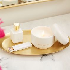 a white candle and some pink flowers on a gold plate with a mirror in the background