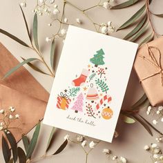 a card with a christmas tree on it next to some wrapping paper and white flowers