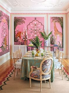 a dining room decorated in pink and green with paintings on the wall, chairs around a round table