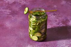 a jar filled with pickles and cucumbers on top of a purple surface