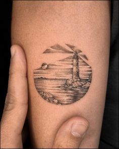 a person is holding their arm with a lighthouse tattoo on it