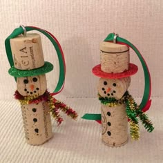 two snowmen made out of wine corks with ribbons and hats on them, one is