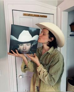 a woman wearing a cowboy hat and holding up a photo with her hands in front of her face