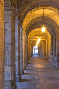 an arched hallway with lights on either side and stone columns at the end that lead into another building