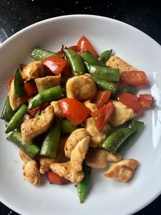 a white plate topped with chicken and veggies on top of a black table