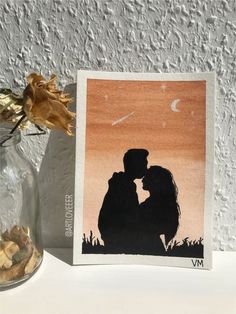 a couple kissing in front of a painting on a wall next to a vase with dried flowers