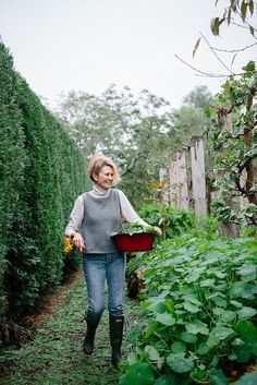 a woman walking through a garden carrying a bucket