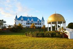 a gazebo in front of a large white house with blue roof and two towers