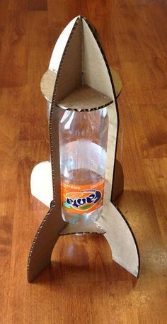 a cardboard rocket ship with a water bottle in it's bottom and an orange label on the side