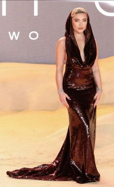 a woman in a brown dress standing on sand