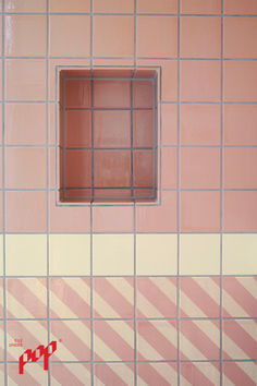 a pink and white tiled wall with a window in the middle that has red stripes on it