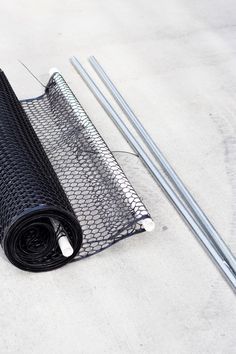 a roll of black wire mesh sitting on top of a cement floor next to two metal poles