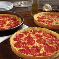 two pepperoni pizzas sitting on top of a wooden cutting board next to other food items