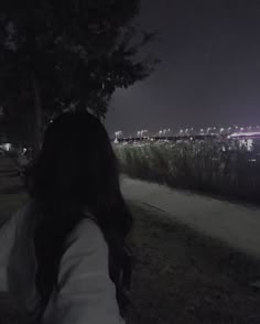 a woman standing in the grass at night with her back turned to the camera, looking out over a city