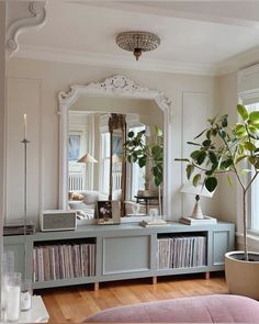 a living room filled with furniture and a large mirror on top of a dresser next to a potted plant