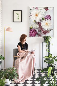 a woman sitting in a chair with a blanket on her lap looking at a magazine