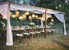 an outdoor wedding setup with white drapes and hanging lanterns