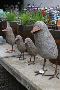 three birds made out of rocks sitting on top of a cement slab next to plants