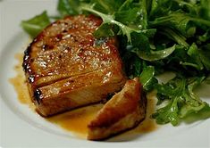 a white plate topped with meat next to a green leafy salad on top of a table