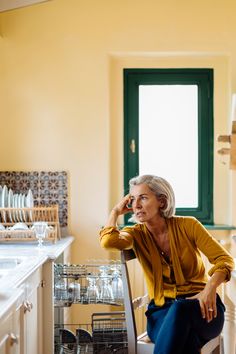 an older woman sitting in a chair next to a kitchen counter with dishes on it