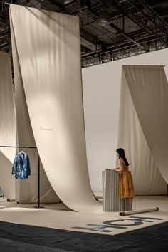 a woman is standing in front of some large white sheets and looking at the clothes on display