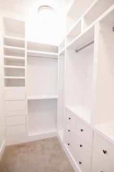 an empty walk in closet with white shelves and drawers on the wall, carpeted floor