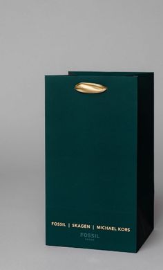 a green paper bag with gold foil on the top and bottom, sitting in front of a gray background