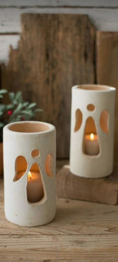 two white candles with holes in them on a wooden table next to potted plants