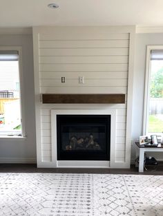 an empty living room with a fireplace and two windows in the wall above it is a rug that has been placed on the floor