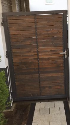 a large wooden gate with metal bars on it's sides and brick walkway leading up to the front door