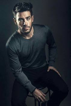 a man sitting on top of a chair in front of a dark background with his hands on his hips