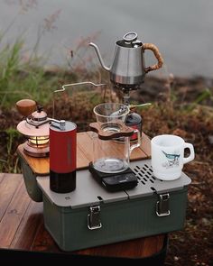 a stove top coffee maker sitting on top of a wooden table next to a lake