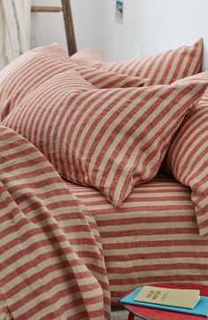 a bed with red and white striped sheets on top of it next to a wooden chair