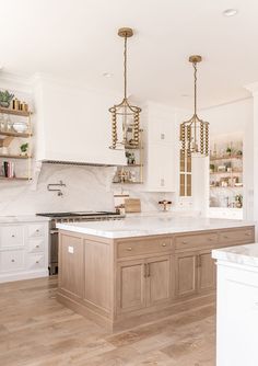 a large kitchen with white cabinets and wooden flooring, two chandeliers hanging from the ceiling