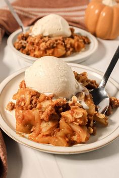 two white plates topped with apple crisp and ice cream next to pumpkins on the table