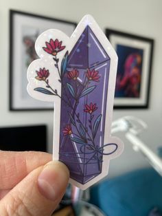 a hand holding up a purple sticker with flowers in the center and an image of a diamond on it