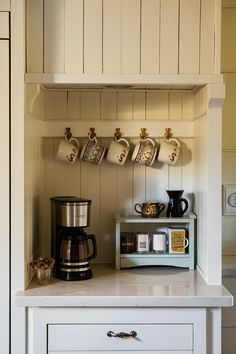 there is a coffee maker and cups on the shelf in this kitchen area with white cabinets