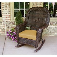 a wicker rocking chair with green cushion next to a flower pot on the patio