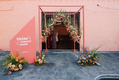 an entrance to a store with flowers and plants in the foreground, next to a pink sign that says smile summer double