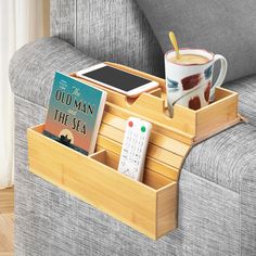 a cup of coffee, remote control and book in a wooden tray on a couch