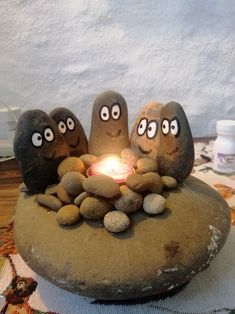 three rocks sitting on top of each other with eyes drawn on them and a lit candle in the middle