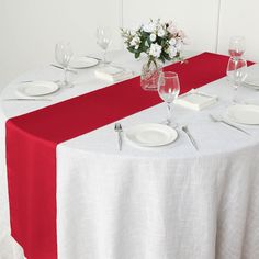 the table is set with white plates, silverware and wine glasses on red cloth