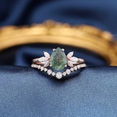 an emerald and diamond ring sitting on top of a blue cloth