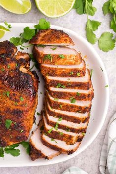 sliced chicken with cilantro garnish on a plate next to limes