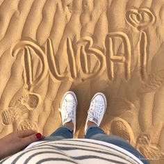 someone's feet in the sand with writing on them