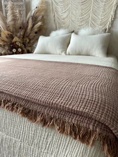 a bed with white and brown blankets on top of it next to a vase filled with flowers