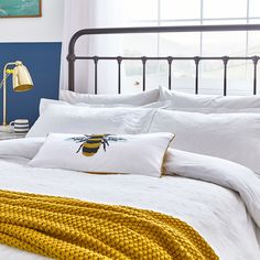 a bed with white sheets and yellow throw pillows on it, next to a blue wall