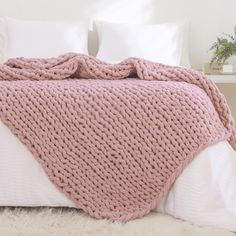 a pink knitted blanket sitting on top of a bed next to pillows and blankets