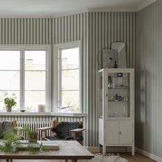 a living room filled with furniture and green striped wallpaper on the walls, along with two large windows